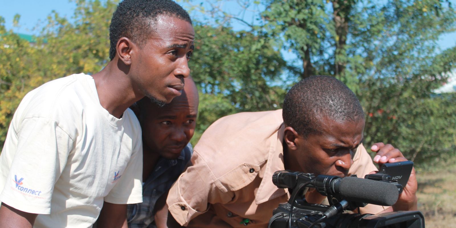 A small film crew filming outdoors with a camera on a tripod