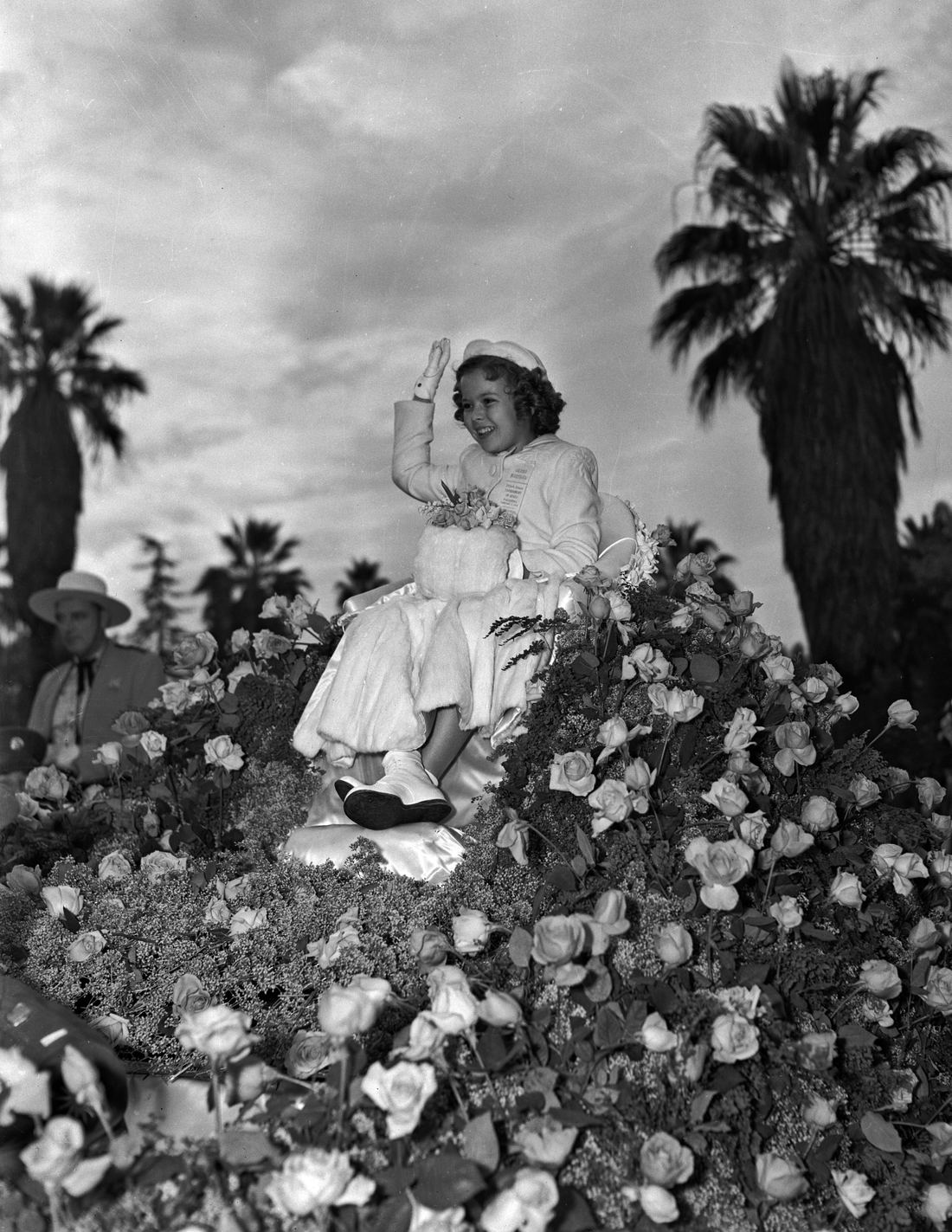 Shirley Temple waving from a flower float at the Rose Parade in 1939
